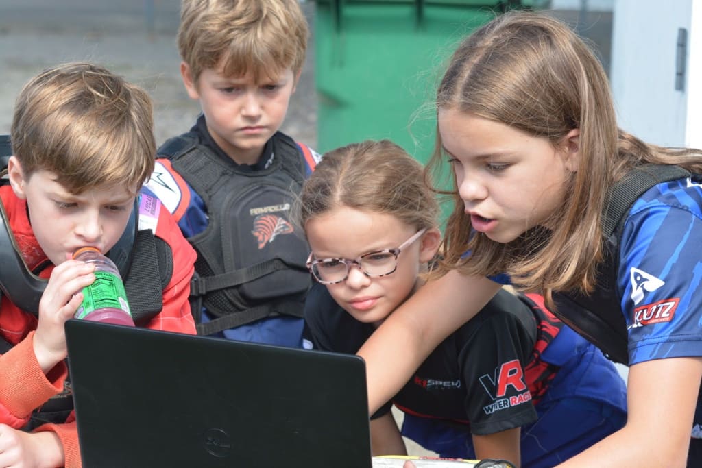 Four young drivers crowd around a laptop to study their lap data.